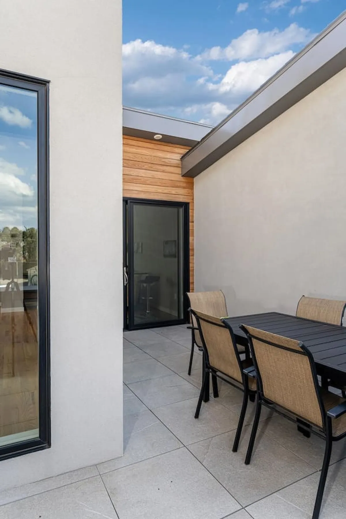 A welcoming outdoor dining area set against a textured wall, with a dining table and chairs perfectly positioned for gatherings. The sliding glass door hints at the seamless transition between the comfort of home and the vibrant streetscape beyond.