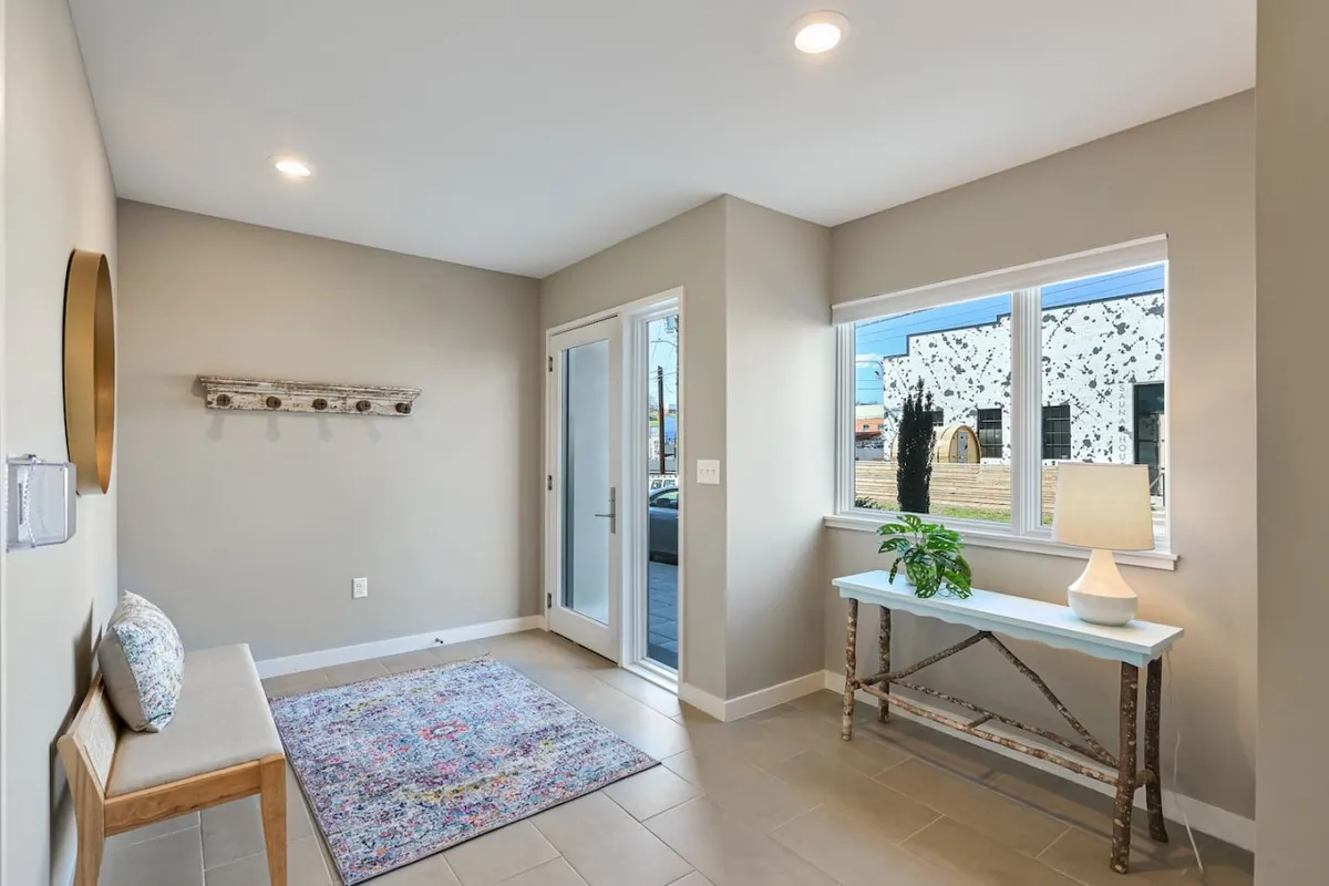 A bright, welcoming interior foyer with a doorway, windows letting in natural light, a plush rug, and a table with a stylish lamp. The space feels open yet secure, perfect for first impressions and easy transitions.